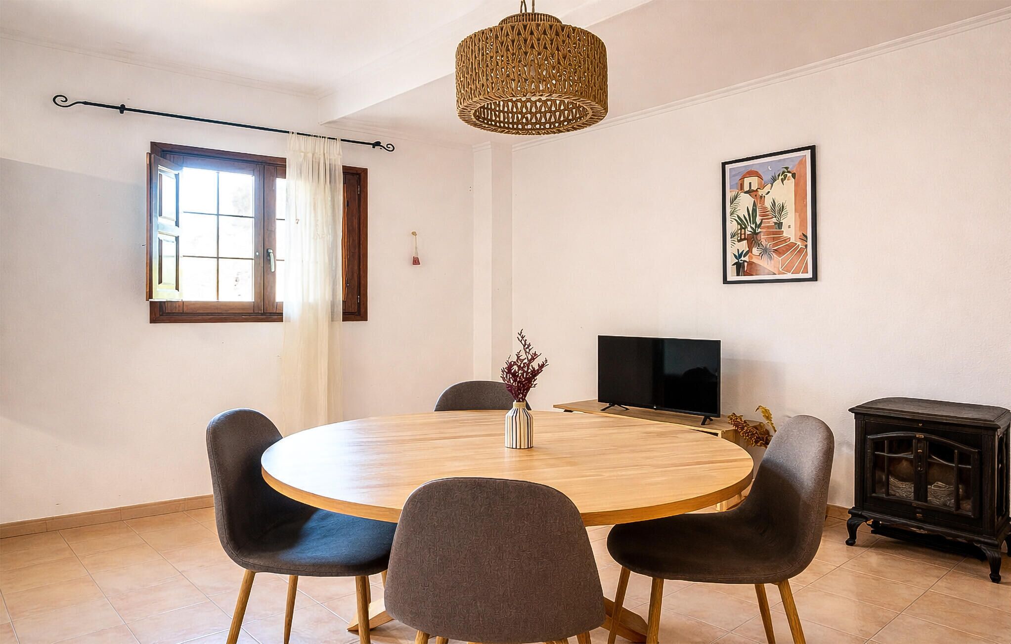 A dining room with a round wooden table, four chairs, a television, and a cabinet.