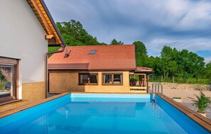 Ett hus med en swimmingpool, ett trädäck och ett rött tegeltak.