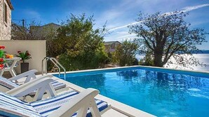 Ein Swimmingpool mit Liegestühlen, blauem Himmel und Blick auf das Meer.