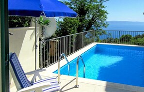 A swimming pool with a view of the sea, a lounge chair, and a blue umbrella. - Amazing home in Makarska (Makarska)