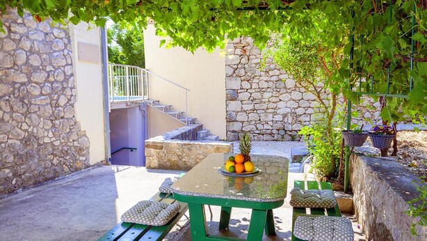 Eine Terrasse mit Tisch für zwei Personen, grünen Bänken und einer Steinmauer.