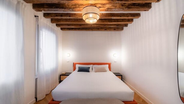 A bedroom with a wooden ceiling, a bed with white bedding, two bedside tables, and a large mirror on the wall. - Cà del Bacino, San Marco (Venice)