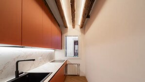 A modern kitchen with a black sink, marble countertop, and orange cabinets. - Cà del Bacino, San Marco (Venice)