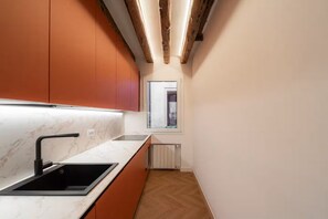 A modern kitchen with a black sink, marble countertop, and orange cabinets. - Cà del Bacino, San Marco (Venice)