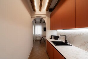 A modern kitchen with a marble countertop, a black sink, and orange cabinetry. - Cà del Bacino, San Marco (Venice)