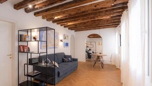 A modern living room with a wooden ceiling, a blue sofa, a black shelving unit, and a dining area with a glass table and chairs. - Cà del Bacino, San Marco (Venice)