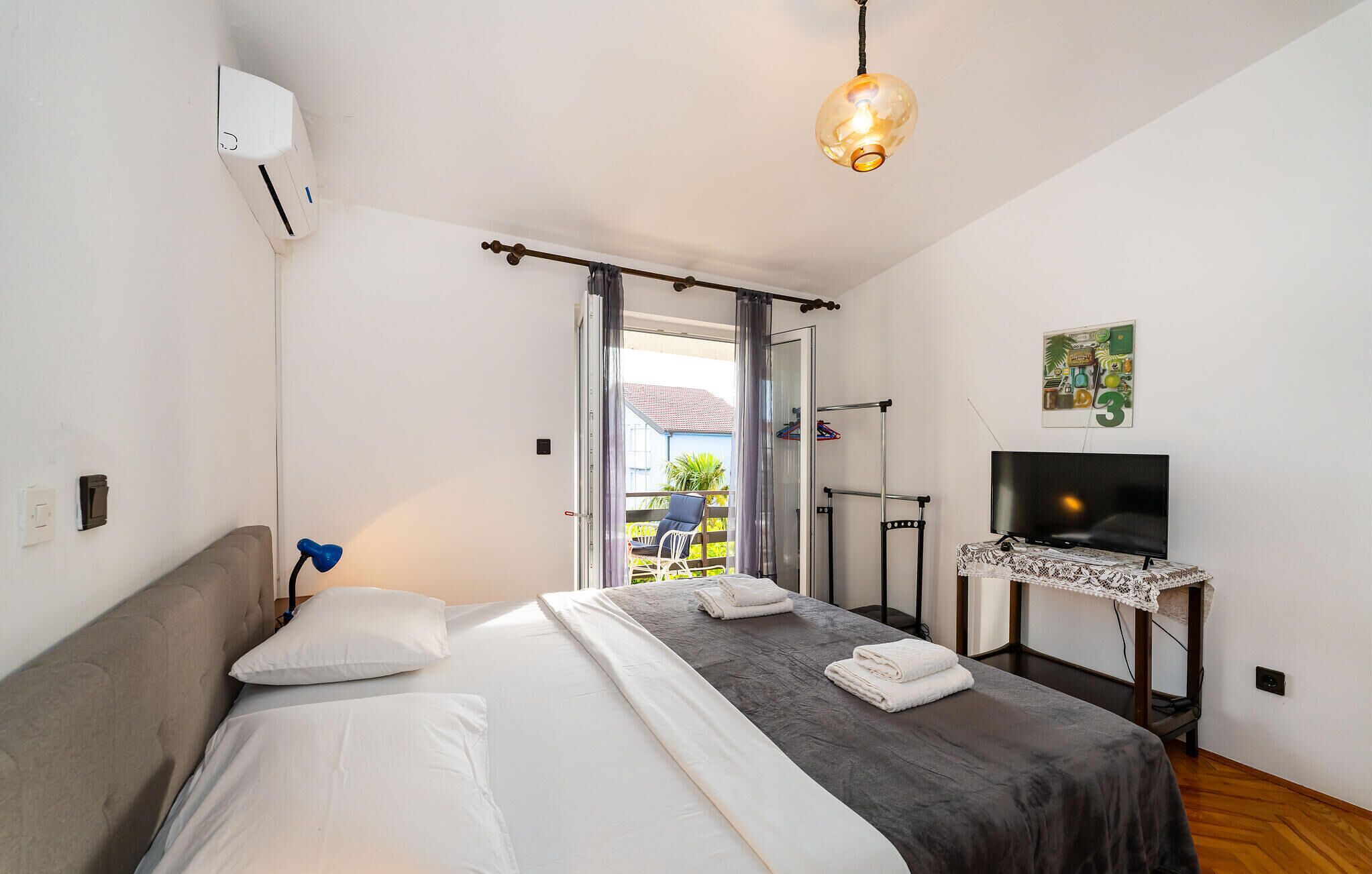 A bedroom with a bed, a TV on a stand, and a balcony with a chair.