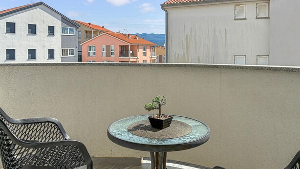 Ein Balkon mit Tisch und Stühlen, einem Blumentopf und Blick auf Gebäude.