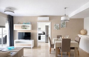 A modern living room with a flat-screen TV, a dining area with a table and chairs, and a kitchen in the background. - Beautiful apartment in Cabanes with house sea view (Cabanes)