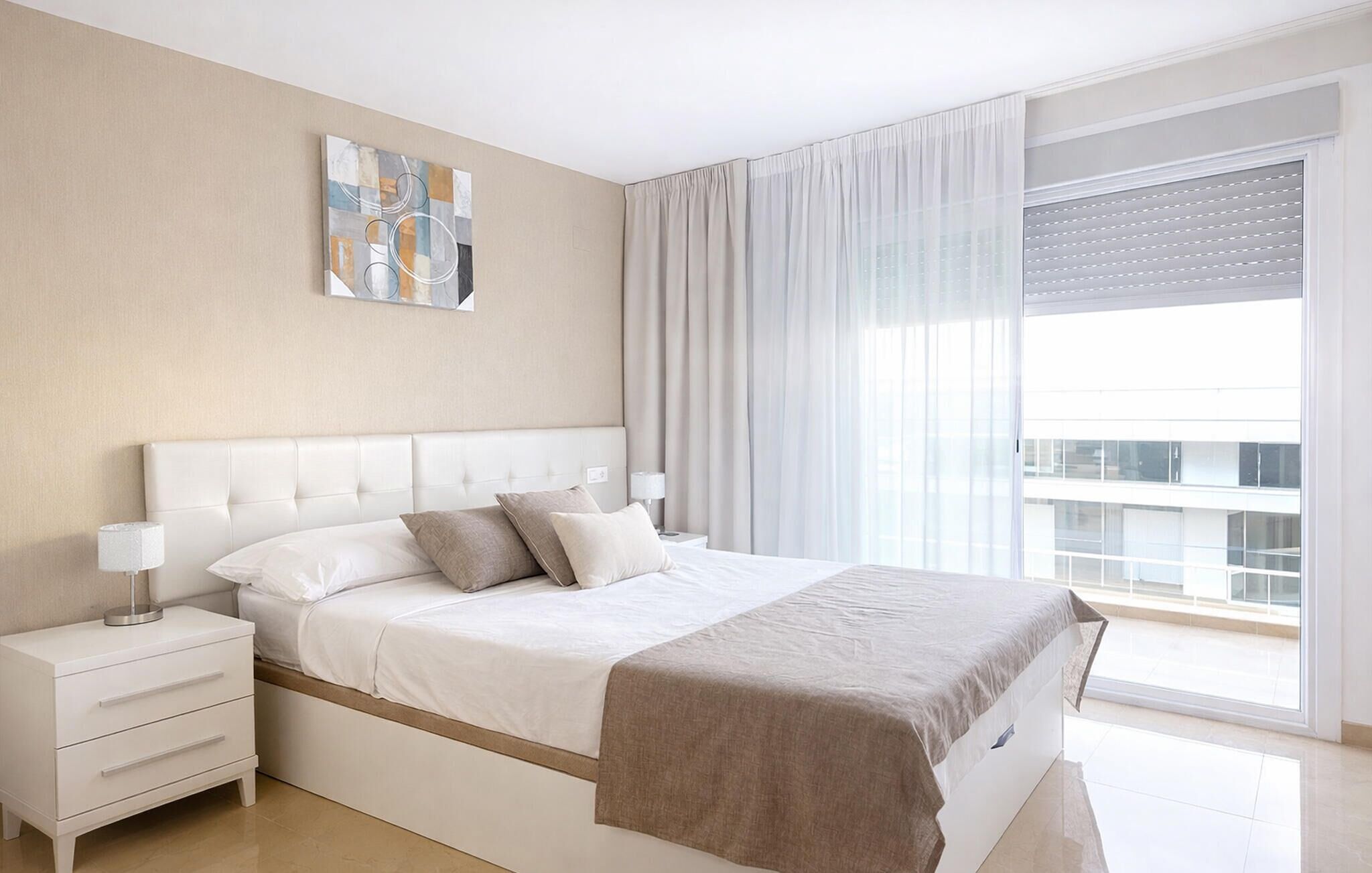 Une chambre à coucher moderne avec un grand lit, une table de chevet, une commode et une fenêtre avec des rideaux.