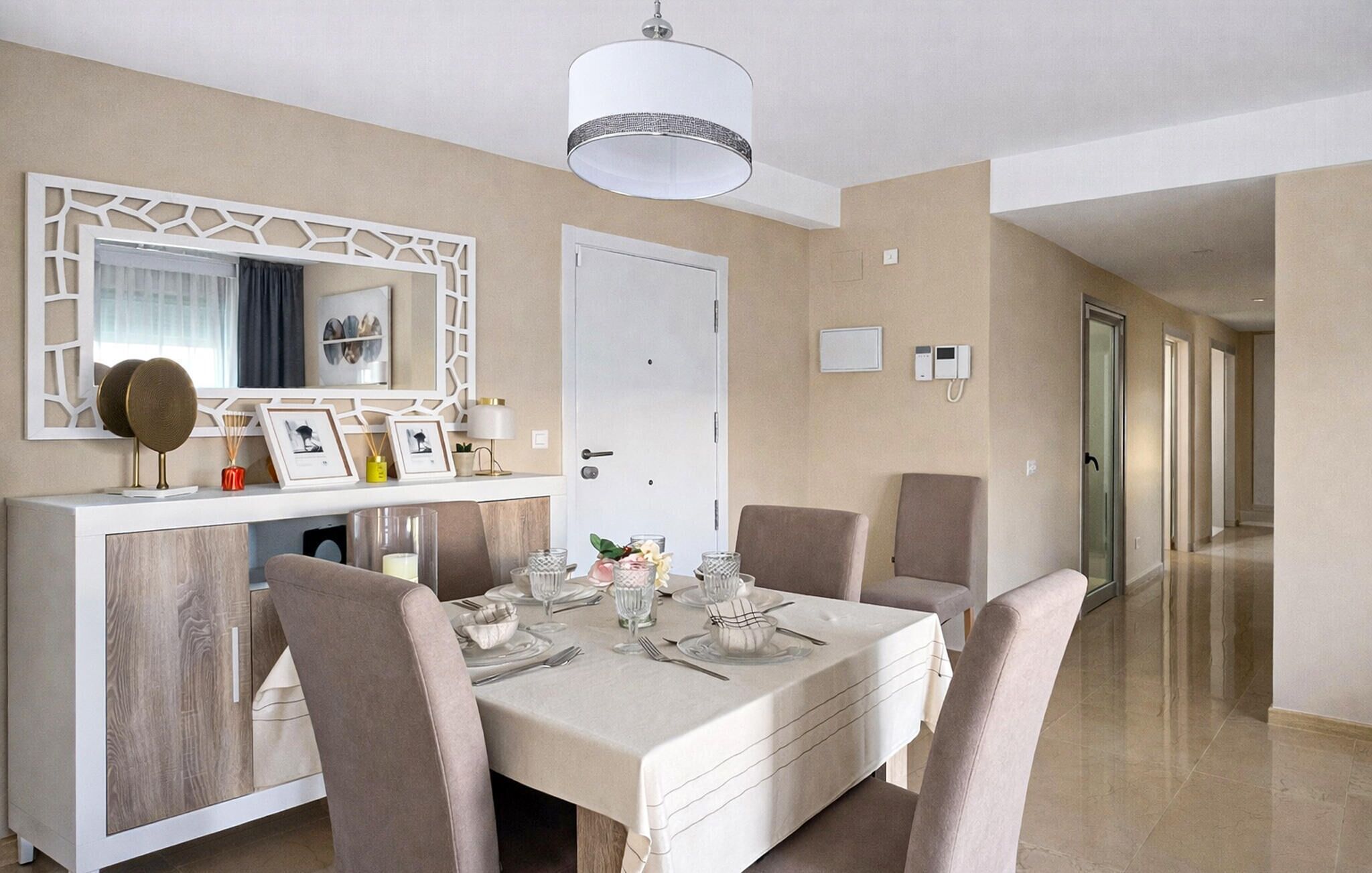 A dining area with a white table set for four, beige walls, a white door, and a hallway with doors.