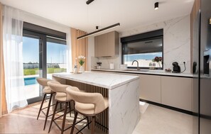 A modern kitchen with a large island, bar stools, and a view of a swimming pool. - Gorgeous home in Policnik (Policnik)