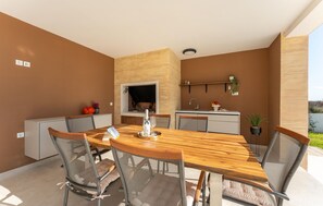 A modern outdoor kitchen with a wooden table and chairs, a built-in grill, and a sink. - Gorgeous home in Policnik (Policnik)