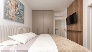 A modern bedroom with a bed, a TV mounted on a wooden panel, and a large abstract painting on the wall. - Luxurious home in Policnik (Policnik)