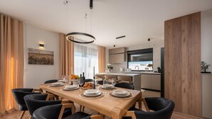 A modern dining area with a wooden table set for six, surrounded by black chairs. A kitchen with a marble countertop and a wooden cabinet is visible in the background. - Luxurious home in Policnik (Policnik)