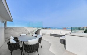 Eine Dachterrasse mit Essbereich, Sitzgelegenheiten im Freien und Blick auf das Meer.