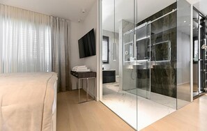 Ein modernes Hotelzimmer mit einem großen Bett, einer begehbaren Dusche, einem Flachbildfernseher und einem Schreibtisch mit Stuhl.