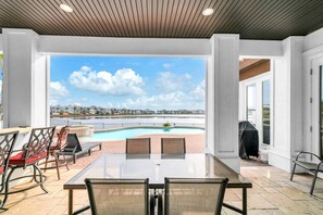 An outdoor patio with a pool, dining table, chairs, and a view of a body of water and distant buildings. - 🦩Book Me Baby! Lakeside Luxury in Destiny East🦩 (Destin)