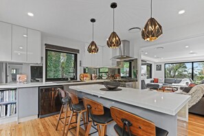 A modern kitchen with a central island, bar stools, and pendant lighting. - Gladstone Luxury Spa Retreat Blue Mountains (Leura)