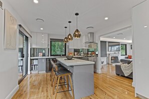 A modern kitchen with a central island, bar stools, pendant lighting, and a fireplace. - Gladstone Luxury Spa Retreat Blue Mountains (Leura)