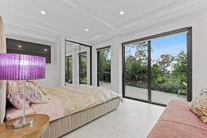 A bedroom with a bed, a nightstand, a lamp, and a sliding glass door leading to a garden. - Gladstone Luxury Spa Retreat Blue Mountains (Leura)