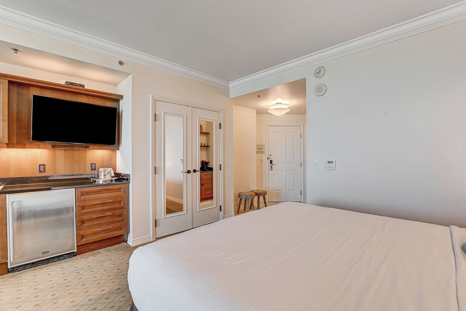 A hotel room with a large bed, a kitchenette with a TV, and a separate bathroom with a mirror and toilet.