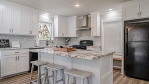 Una cocina con armarios blancos, un refrigerador negro y una encimera de mármol.