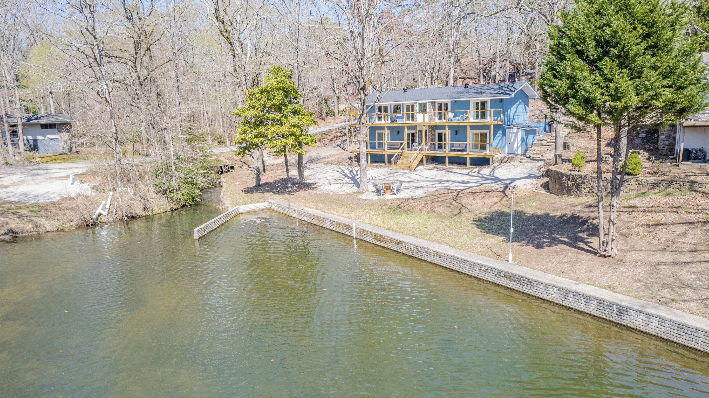 A two-story house with a deck, surrounded by trees and a pond.