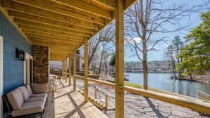 Un espacio al aire libre techado con una terraza de madera, una pared de piedra y vistas a un lago.