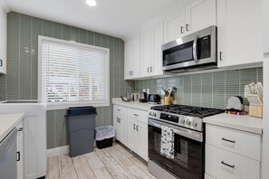 Una cocina moderna con armarios blancos, estufa de acero inoxidable, microondas y una ventana con persianas.