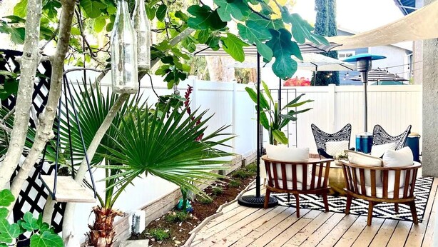 Un terrazzo in legno con mobili da esterno, immerso nel verde e circondato da un recinto bianco.