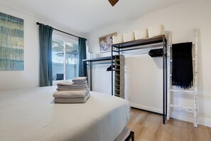 Un dormitorio con una cama litera, una cama con una pila de toallas, una ventana con cortinas y un cuadro en la pared.