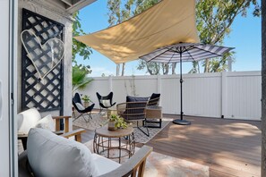 Een terras buiten met rieten meubels, een ronde tafel met een plant in pot en een grote gestreepte parasol.