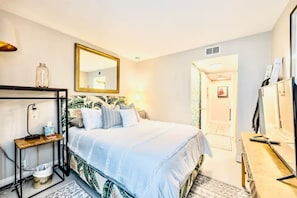 Une chambre à coucher comprenant un lit, une table de chevet, une lampe, un miroir et un meuble pour la télévision.