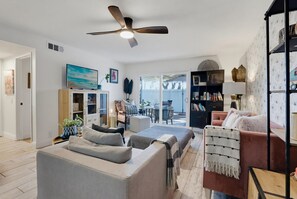 Een moderne woonkamer met een bank, een bijzettafeltje, een plafondventilator en een boekenplank.