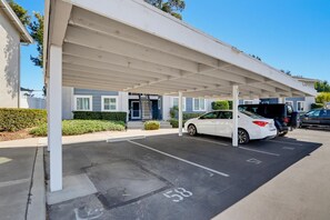 A covered parking area with a car and a truck, a building with a blue facade, and a clear sky. - Artful Plant-Filled Beach Rtreat W/ Pvt Backyard and 8 minutes from the Beach!! (Laguna Niguel)
