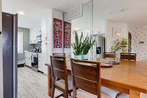 A modern kitchen with white cabinets, a stainless steel refrigerator, and a dining area with a wooden table and chairs. - Artful Plant-Filled Beach Rtreat W/ Pvt Backyard and 8 minutes from the Beach!! (Laguna Niguel)