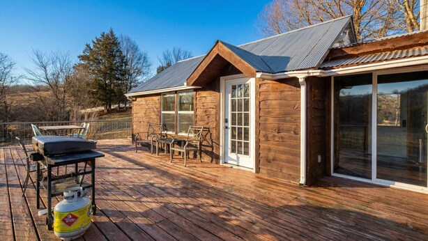 Une cabane en bois avec une terrasse, un barbecue et une bouteille de propane.