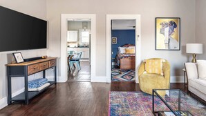 Un salon moderne avec un téléviseur à écran plat, une table basse, un fauteuil jaune et un tapis coloré.