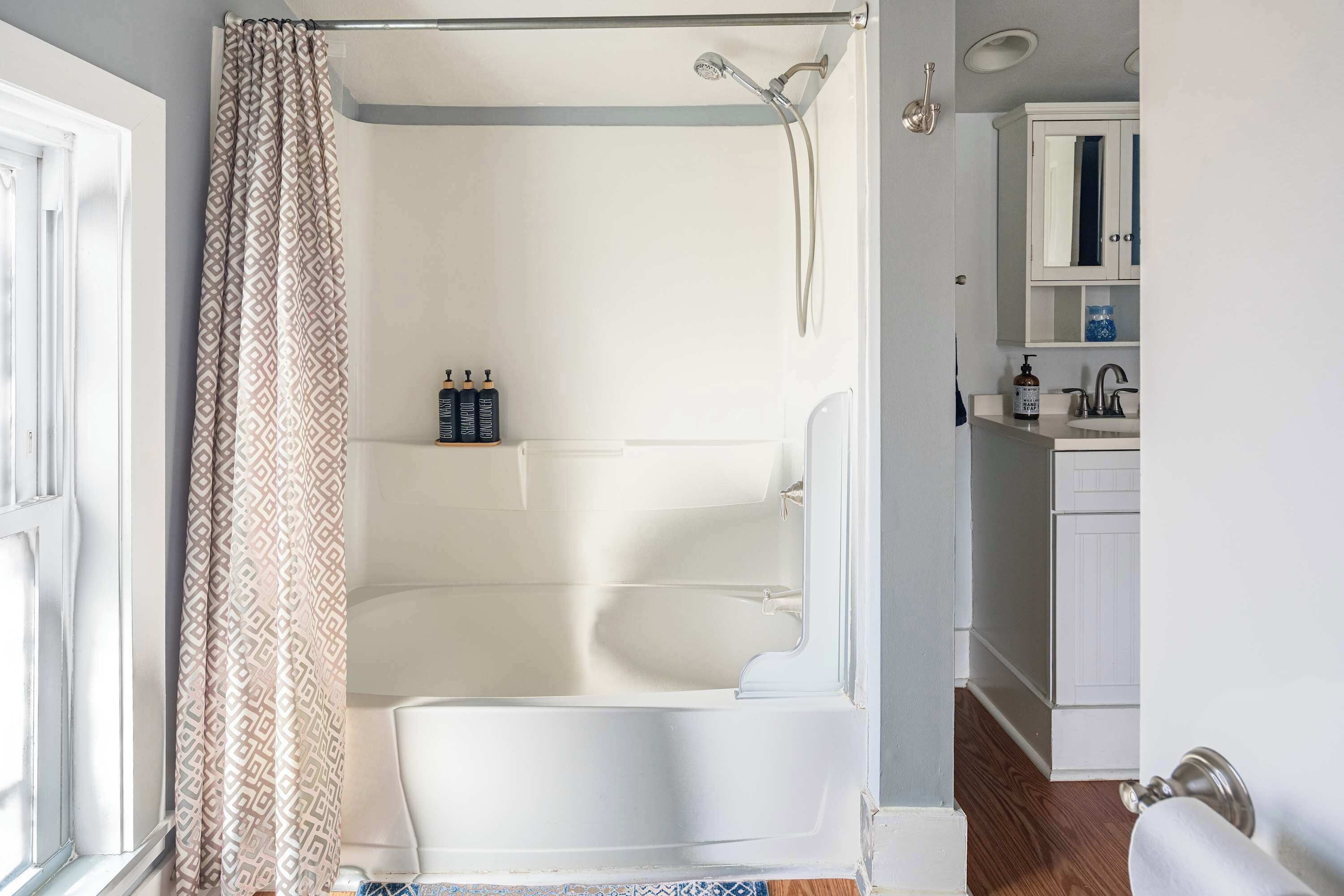 Un bagno con vasca, doccia e servizi igienici. Sulla borsa del sapone ci sono articoli da toilette e una finestra con tenda.