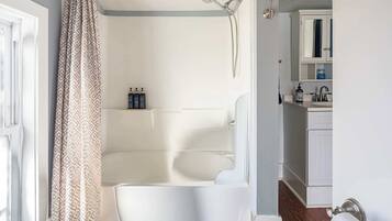 Un bagno con vasca, doccia e servizi igienici. Sulla borsa del sapone ci sono articoli da toilette e una finestra con tenda.