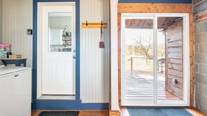 Une porte en bois avec un panneau blanc, une petite étagère sur laquelle sont posés quelques objets, et une vue sur une terrasse en bois à l’extérieur.