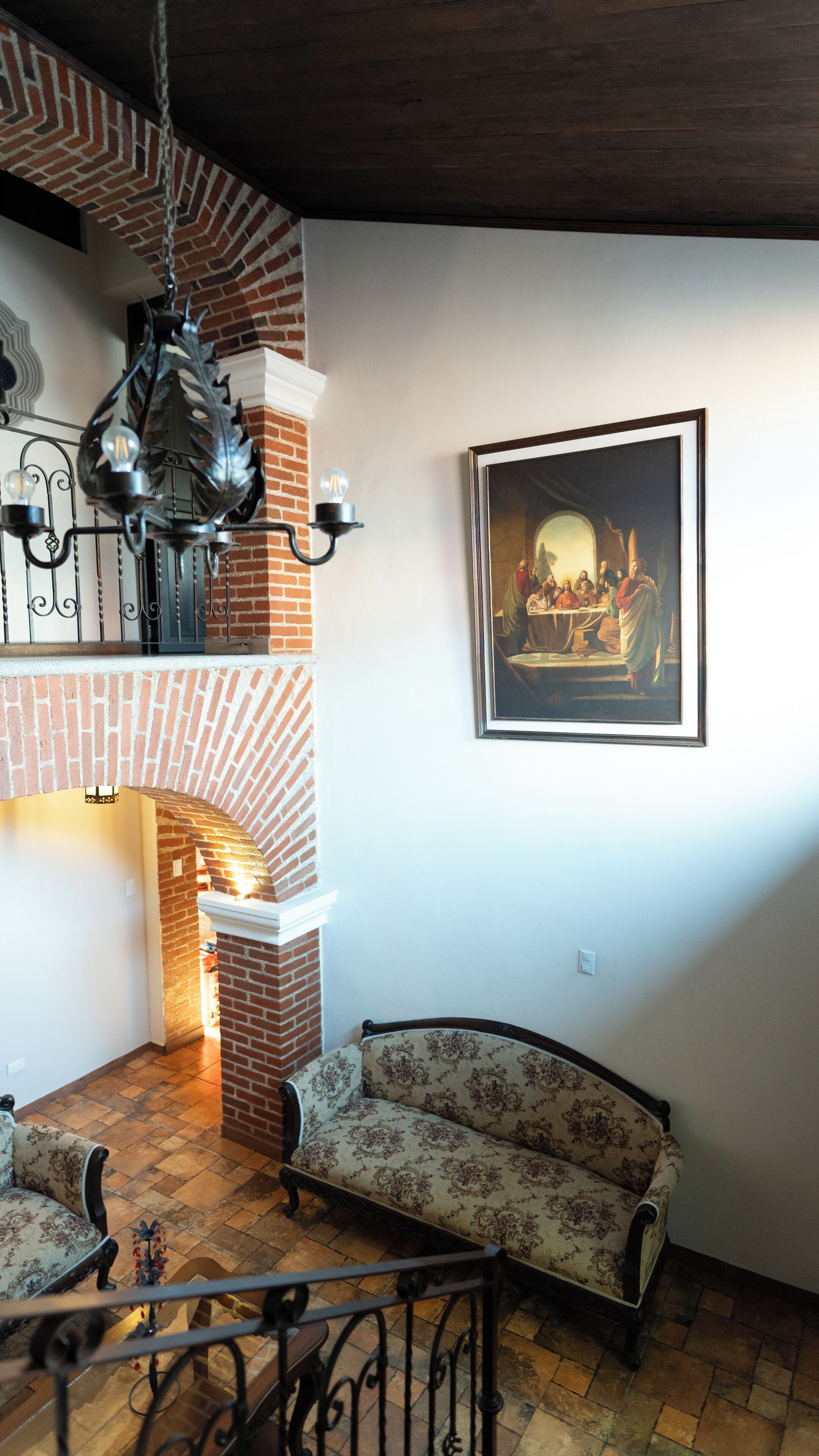 Una stanza con camino in mattoni, un divano, un lampadario e un quadro appeso al muro.