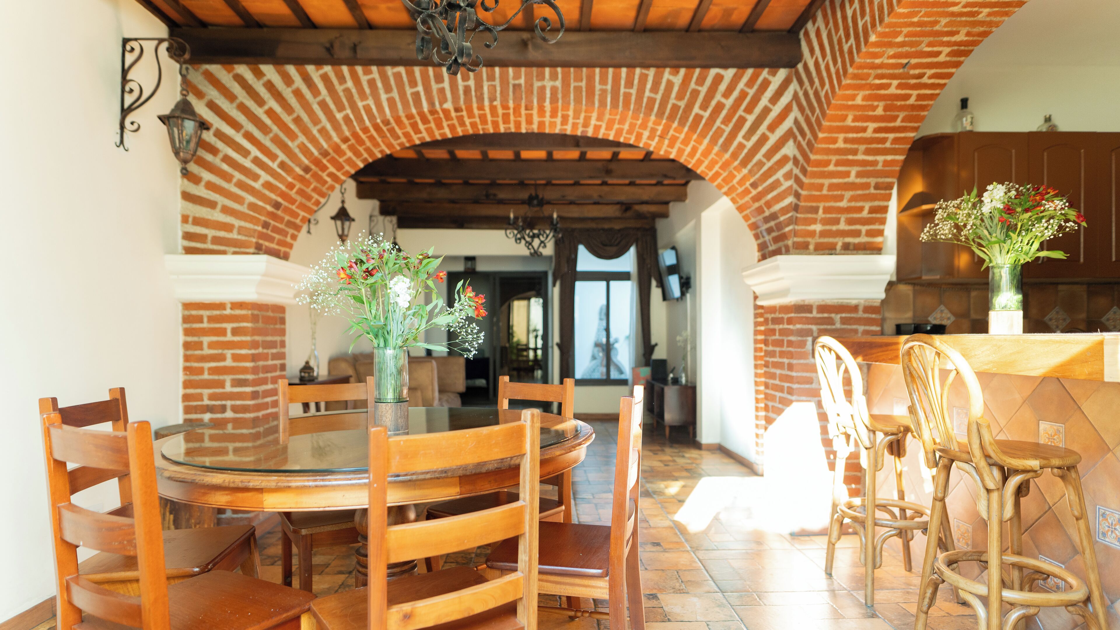 A dining area with a brick archway, wooden chairs, a round table, and a vase with flowers.