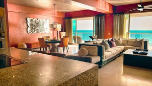 Un salon moderne avec un grand canapé, un coin repas avec des chaises et une vue sur la mer grâce à de grandes fenêtres.