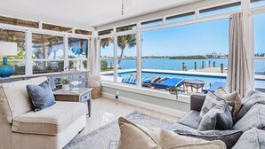 Ein geräumiges Wohnzimmer mit großem Fenster mit Blick auf einen Pool und das Meer.