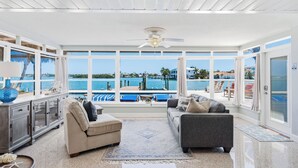 Ein geräumiges Wohnzimmer mit großem Fenster und Blick auf einen Pool und den Ozean.