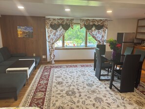 A living room with a sofa, a dining table with chairs, a patterned rug, and curtains over a window. - Experience comfort in our Danvers, MA cute private studio . (Danvers)