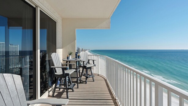 Een balkon met uitzicht op zee, een tafel met stoelen en een bloempot.
