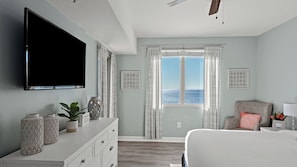 A bedroom with a TV, a dresser, a bed, a window with a view, and a ceiling fan. - Emerald Horizon by Avantstay Beachfront Condo + Resort Pool + Gulf Balcony Views + Near Pier Park & Dining (Panama City Beach)